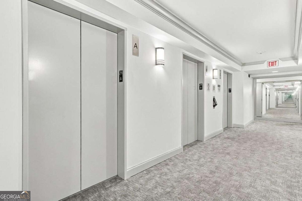 Condominium hallway with several elevators, gray carpet, and a long corridor extending into the distance.