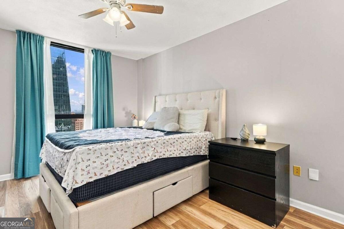 Bedroom with a tufted bed, turquoise curtains, and a city high-rise visible through the window.