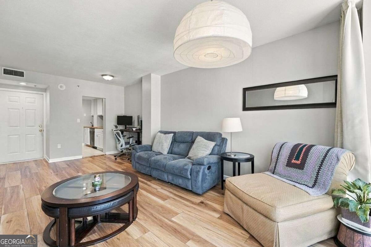 Furnished condo living room with blue sofa, beige armchair, and wood-look floors.