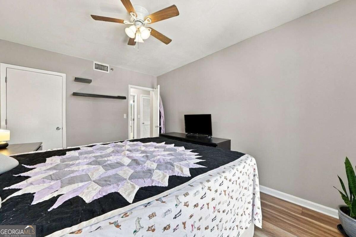 Bedroom with a geometric quilt, wood-blade ceiling fan, television, and potted snake plant.