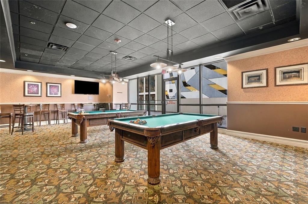Billiards room with two pool tables, bar stools, and patterned carpet.