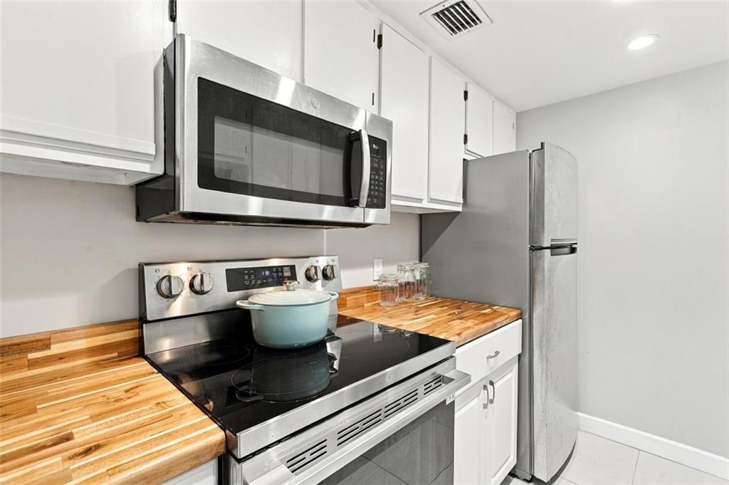 Modern kitchen with stainless steel appliances, white cabinets, and butcher-block countertops.
