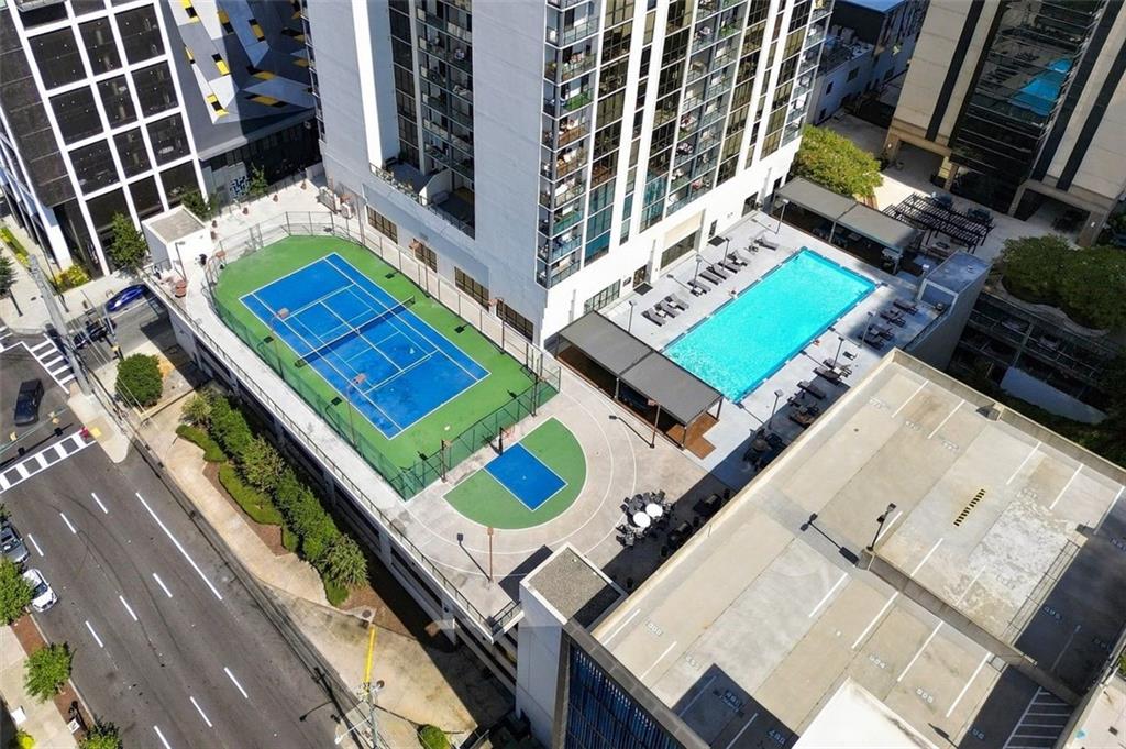 Aerial view of a high-rise condominium’s amenity deck with a pool, tennis court, and basketball court.