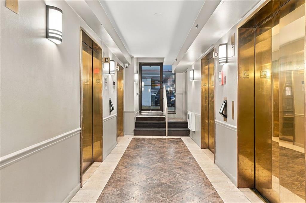 Elevator lobby with brass doors, marble flooring, and a short stairway.