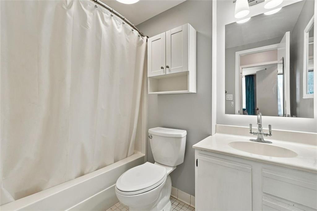 Bathroom with a curtained tub and shower, toilet, and white vanity beneath a large mirror.