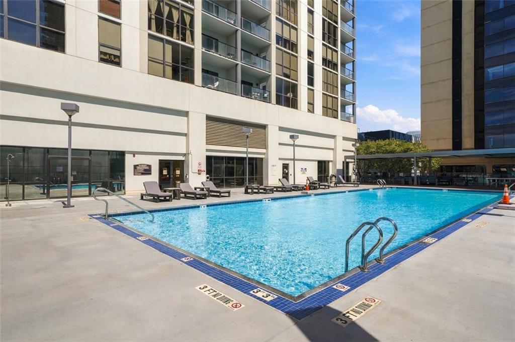 Outdoor pool beside a high-rise condominium, with lounge chairs and glass balconies.