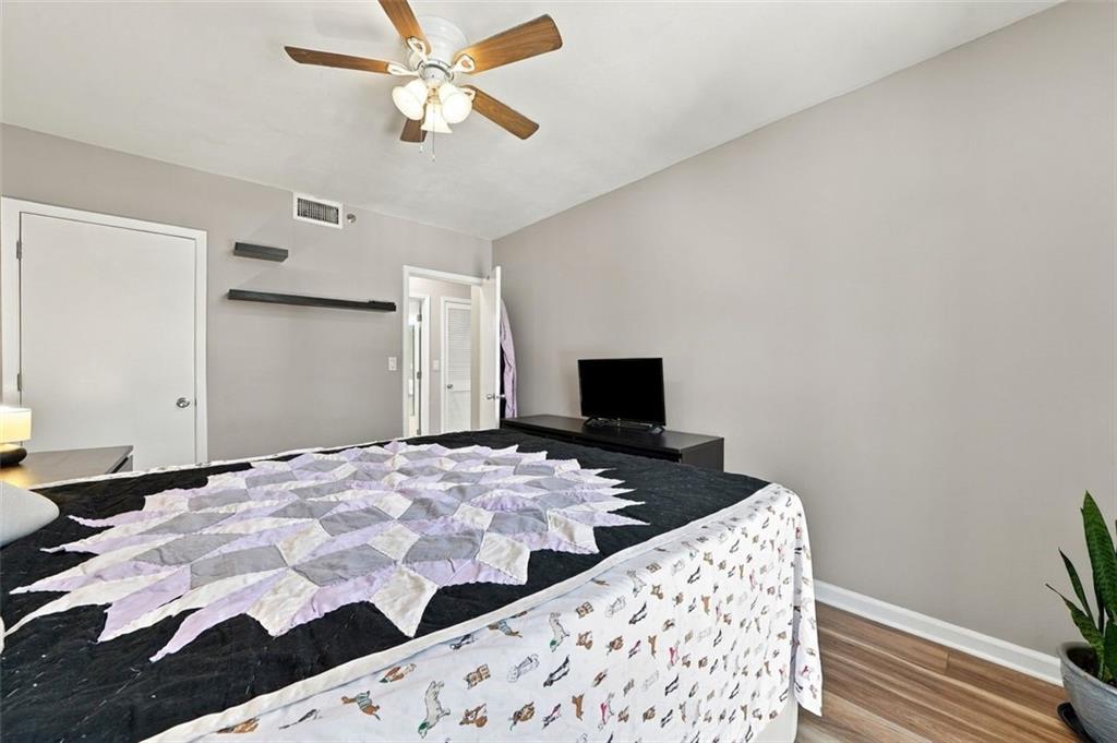 Bedroom with a large lavender-and-black quilted bed, ceiling fan, and television on a low dresser.