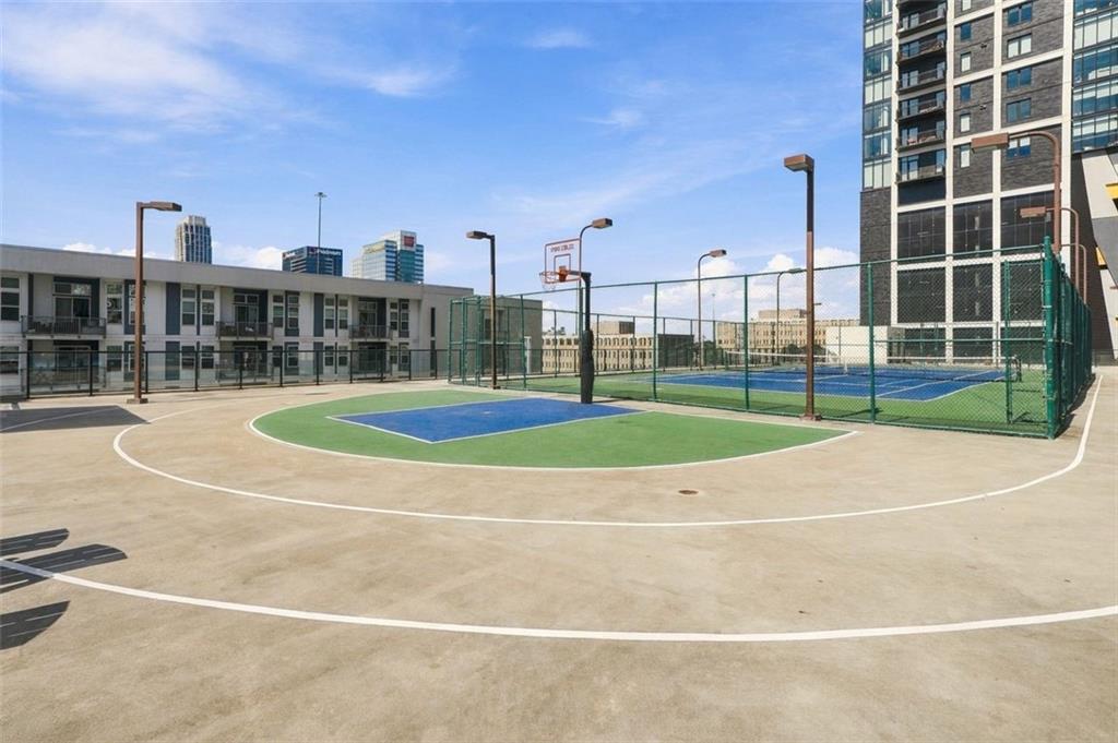 Outdoor basketball court beside a fenced tennis court, with Atlanta’s skyline in the distance.