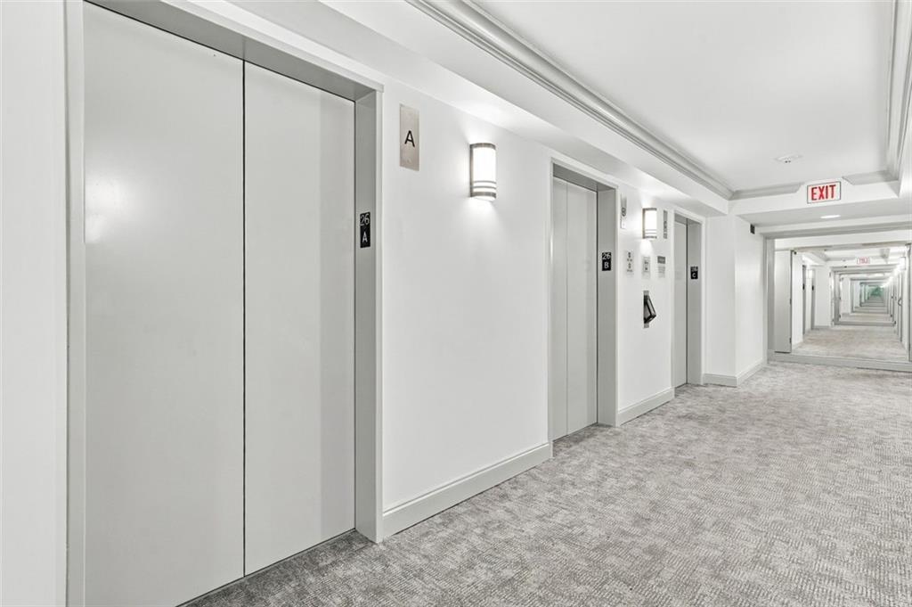 High-rise hallway with elevator doors, gray carpet, and wall sconces.