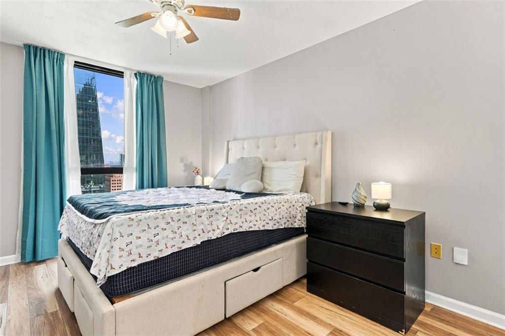 Bedroom with a beige upholstered bed, teal curtains, and a city view through the window.