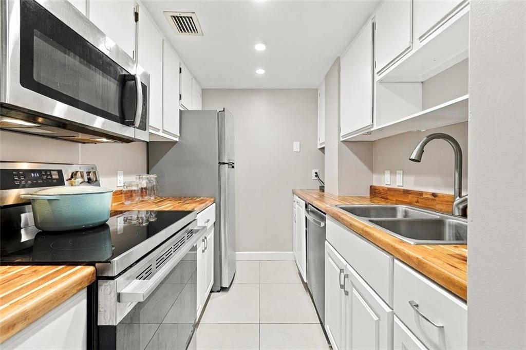 Narrow kitchen with butcher-block counters, stainless appliances, and a double-basin sink.