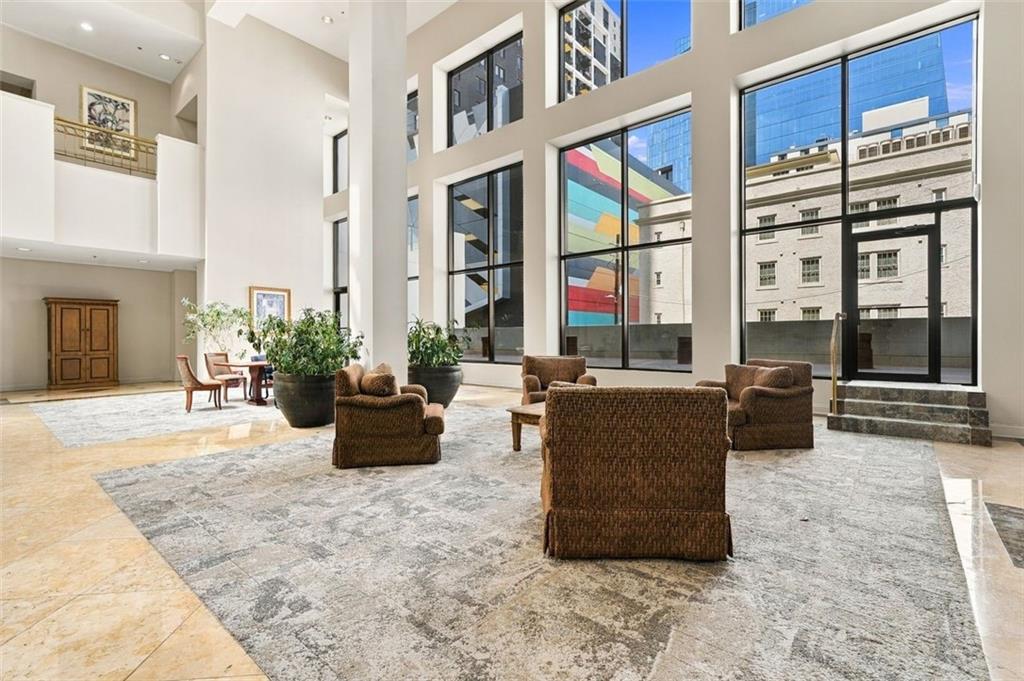Double-height lobby with floor-to-ceiling windows, potted plants, and brown lounge seating.
