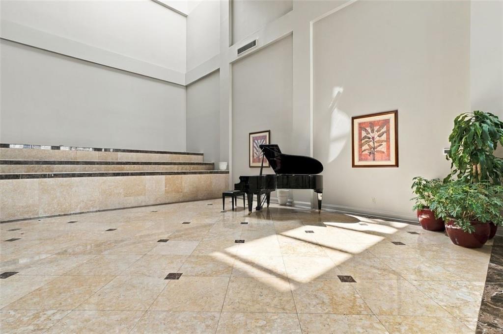 Building lobby with a black grand piano, polished stone floor, and potted plants.