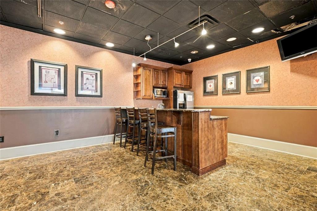 Amenity room with a wood-paneled bar, stools, kitchenette appliances, and framed wall art.