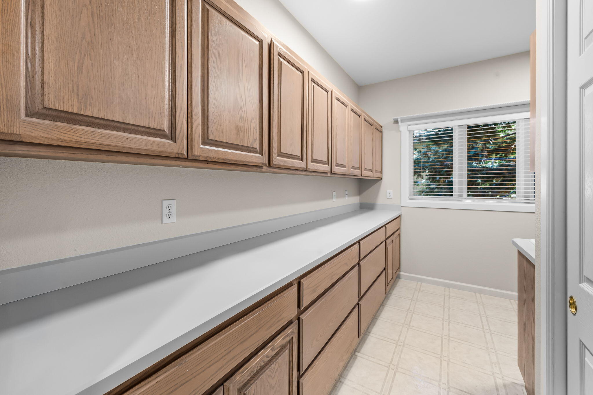 Utility room with long countertops, extensive wood cabinetry, tiled floor, and a window with blinds.