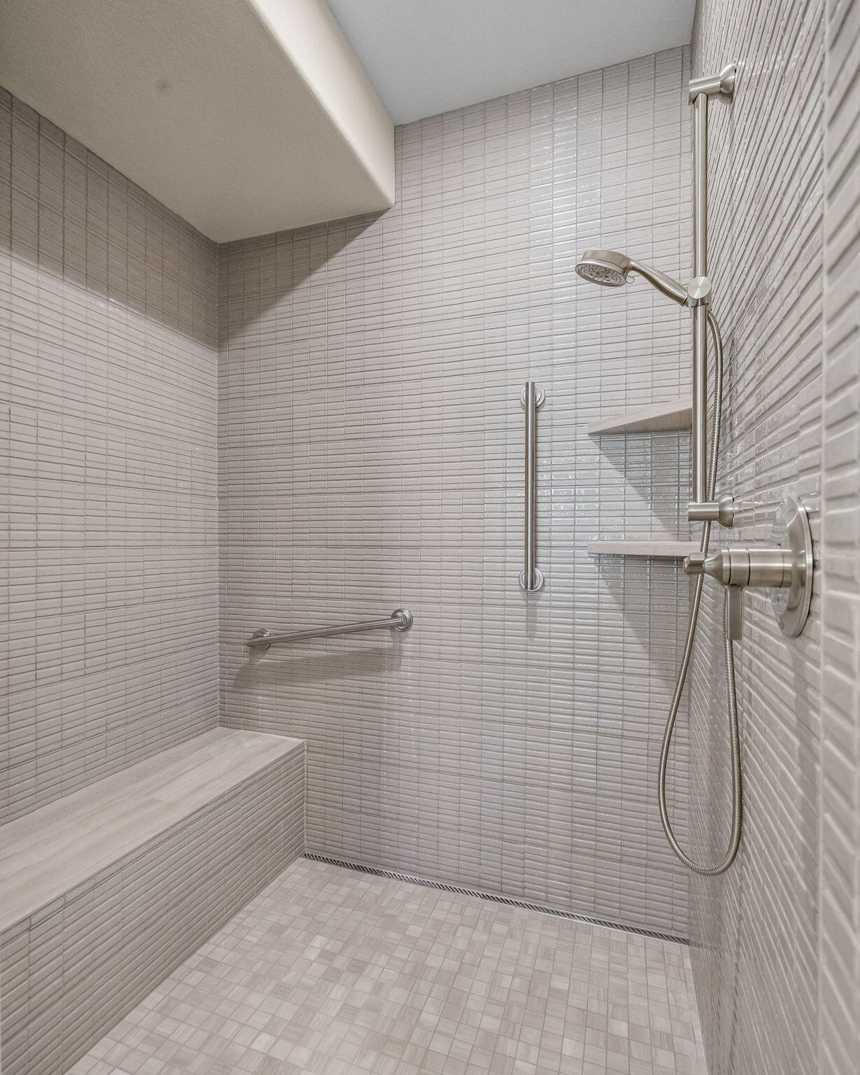 Walk-in shower with a built-in tiled bench, grab bars, and handheld showerhead.