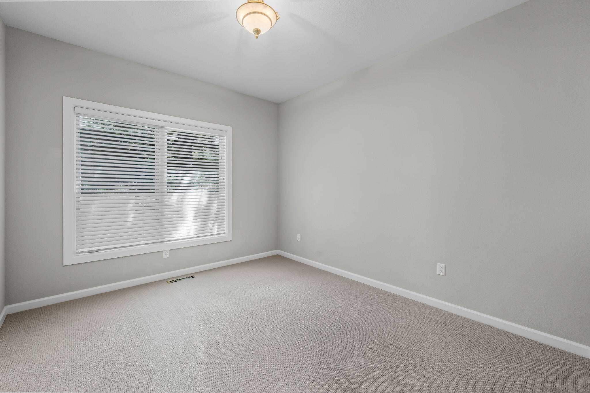 Empty bedroom with beige carpet and a large window covered by white blinds.