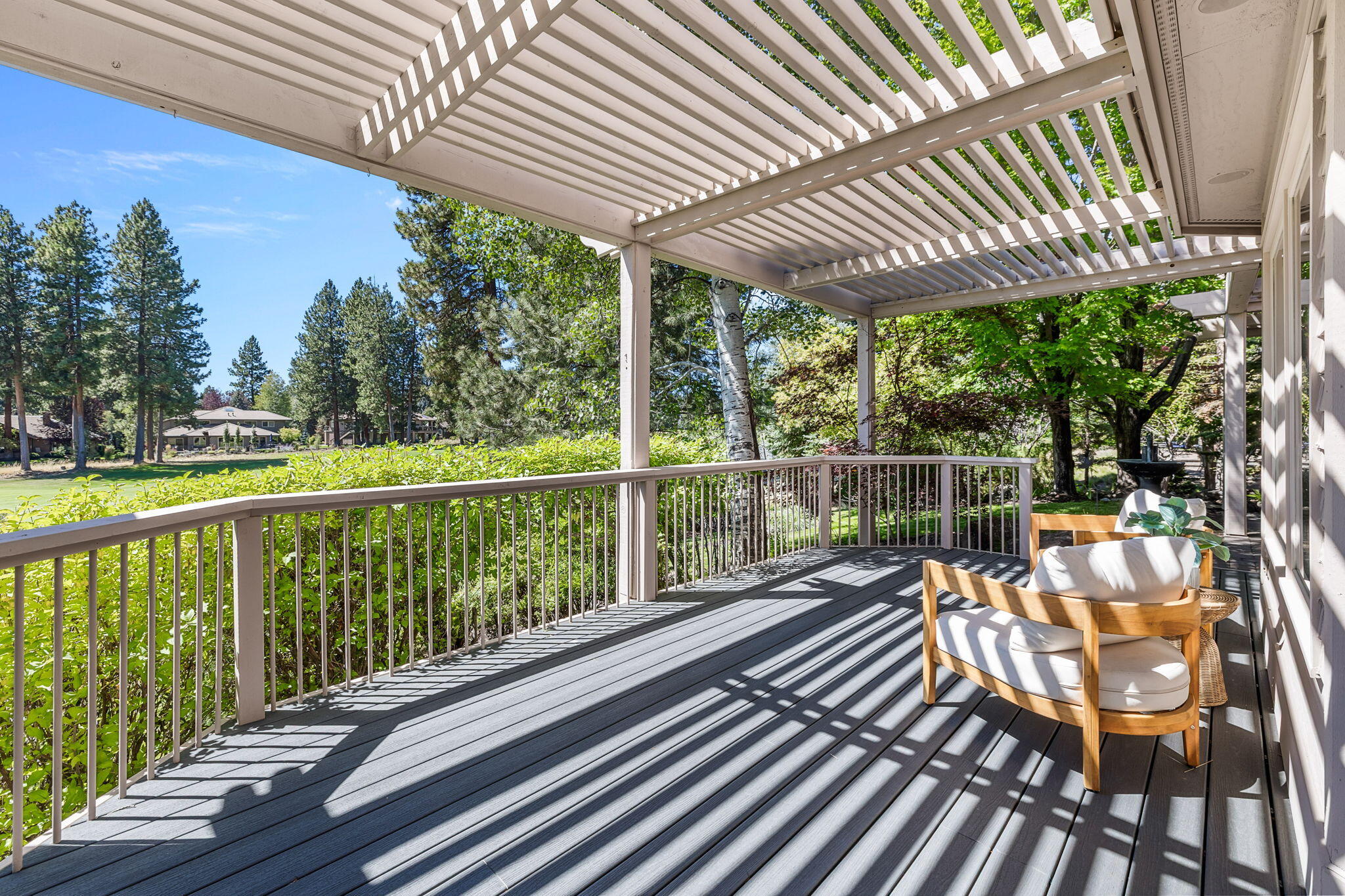 Covered deck with pergola shade, cushioned chairs, and leafy views over a grassy lawn.