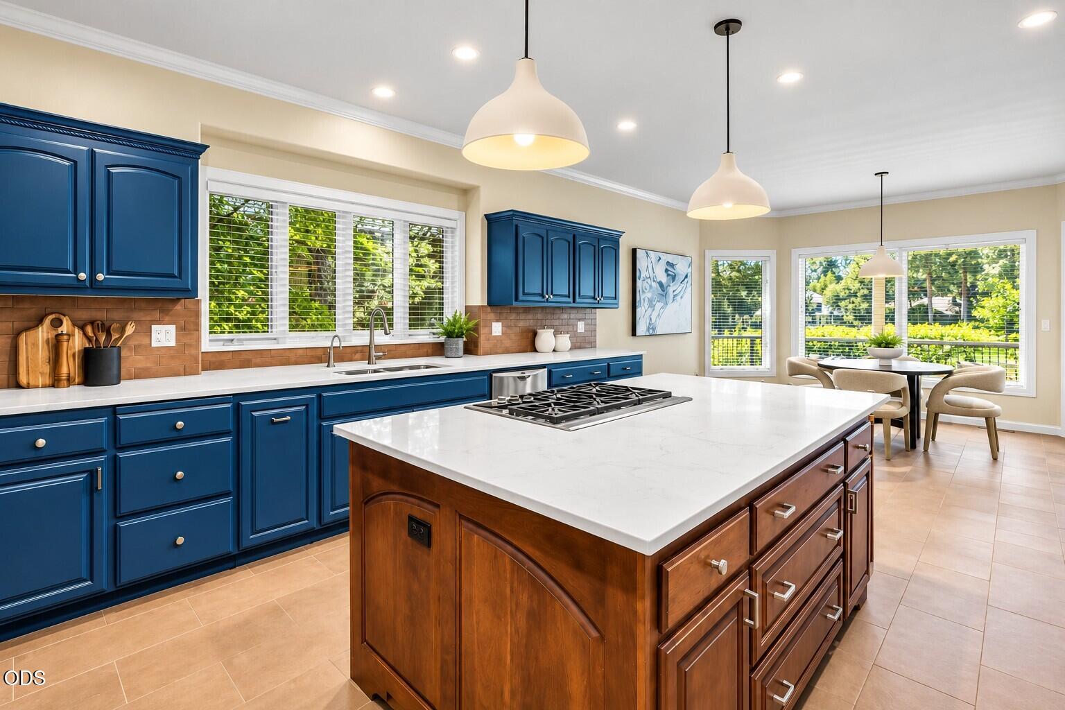 Kitchen with deep blue cabinets, a large wood island, and a gas cooktop beside a sunny dining area.