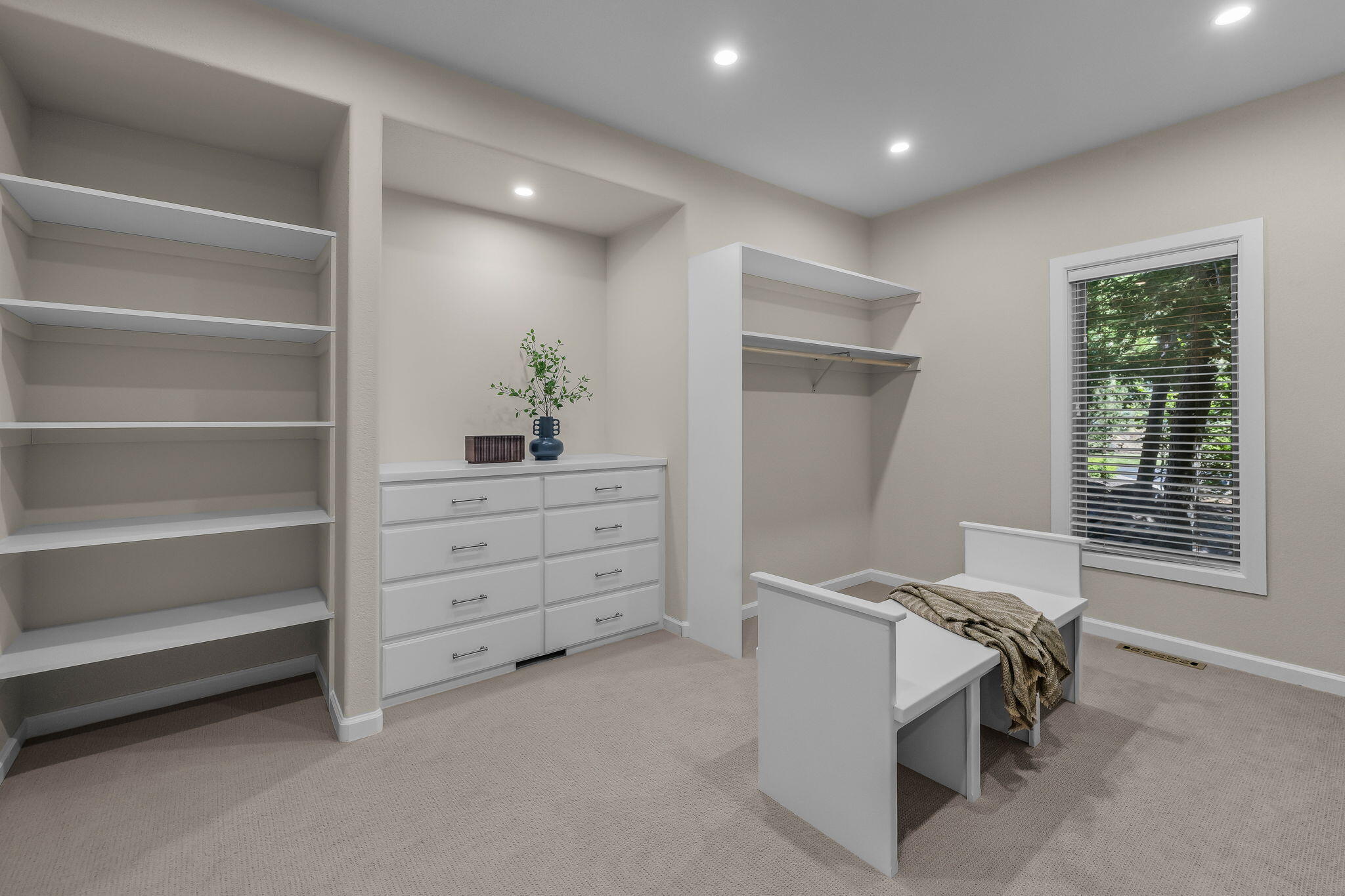 Walk-in closet with built-in white shelving, drawers, and a bench beside a window.