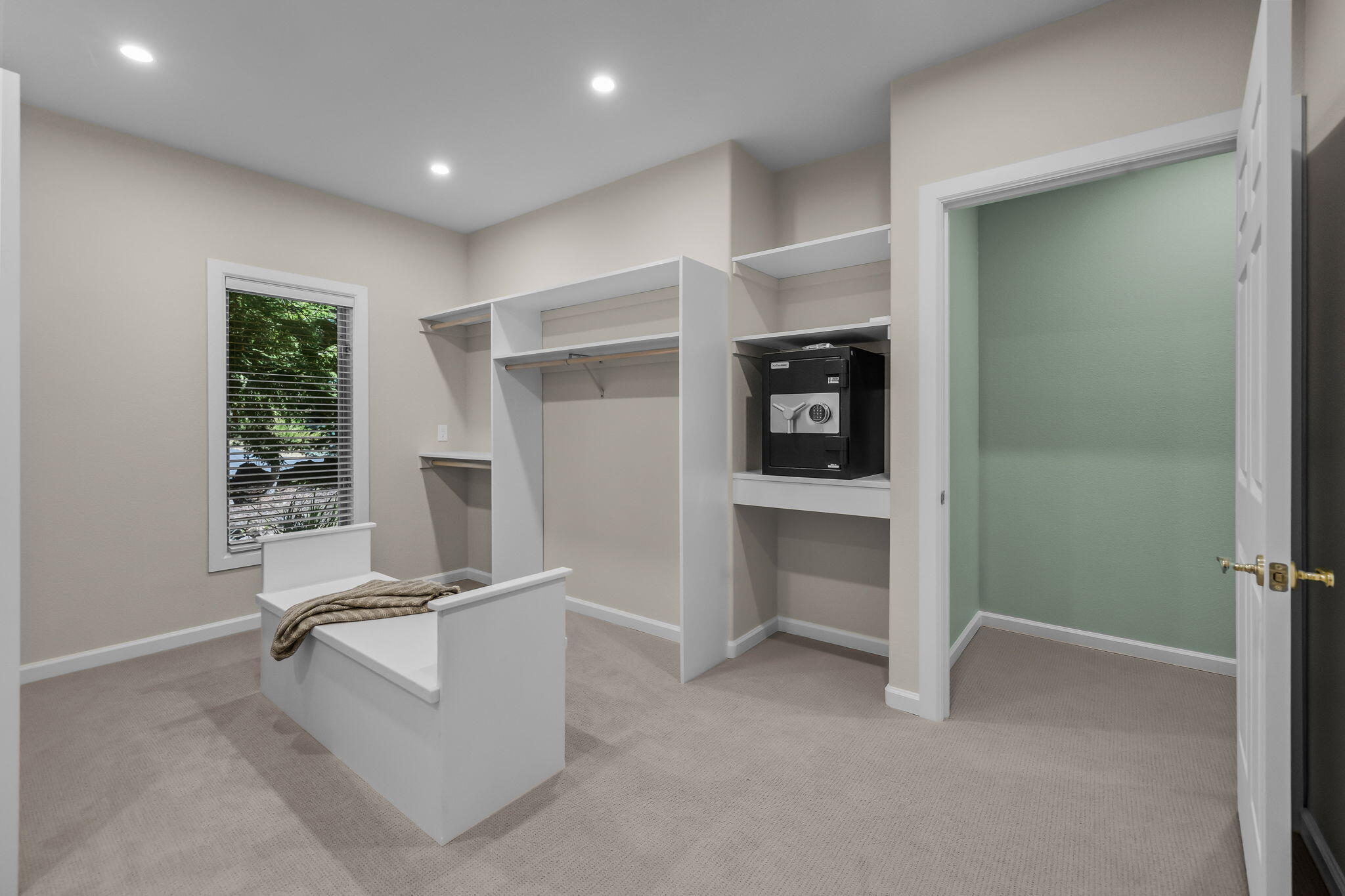 Walk-in closet with built-in shelving, a recessed safe, and a white bench beneath a window.