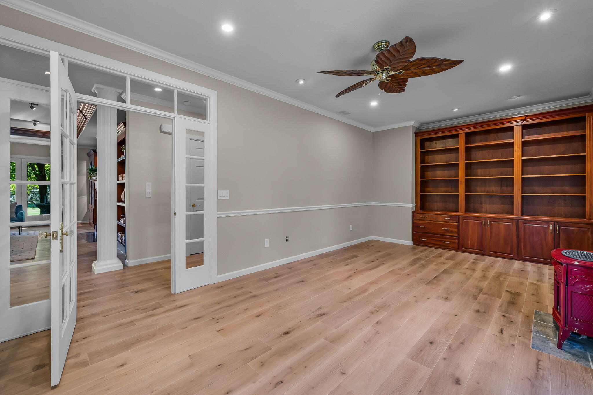 Room with built-in wood bookcases, light plank flooring, and glass-paneled French doors.
