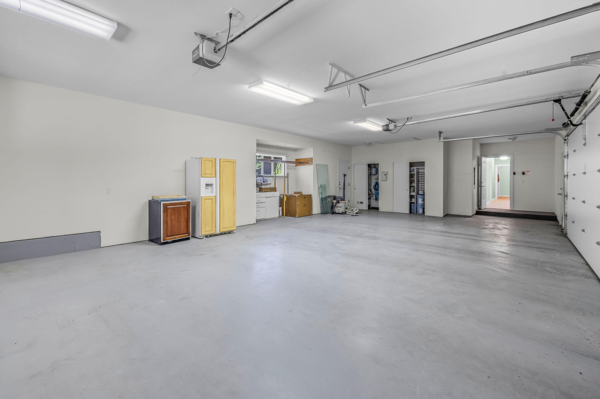 Spacious garage with a broad concrete floor, overhead door tracks, and cabinets along the back wall.