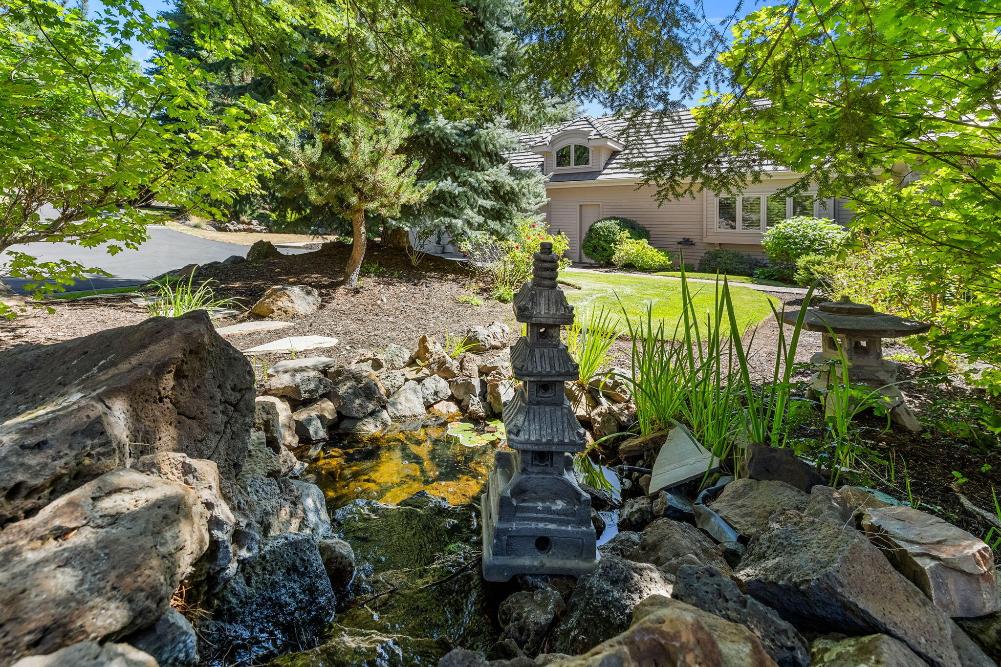 Landscaped front yard with a rock-edged pond and stone lantern beside a beige house.