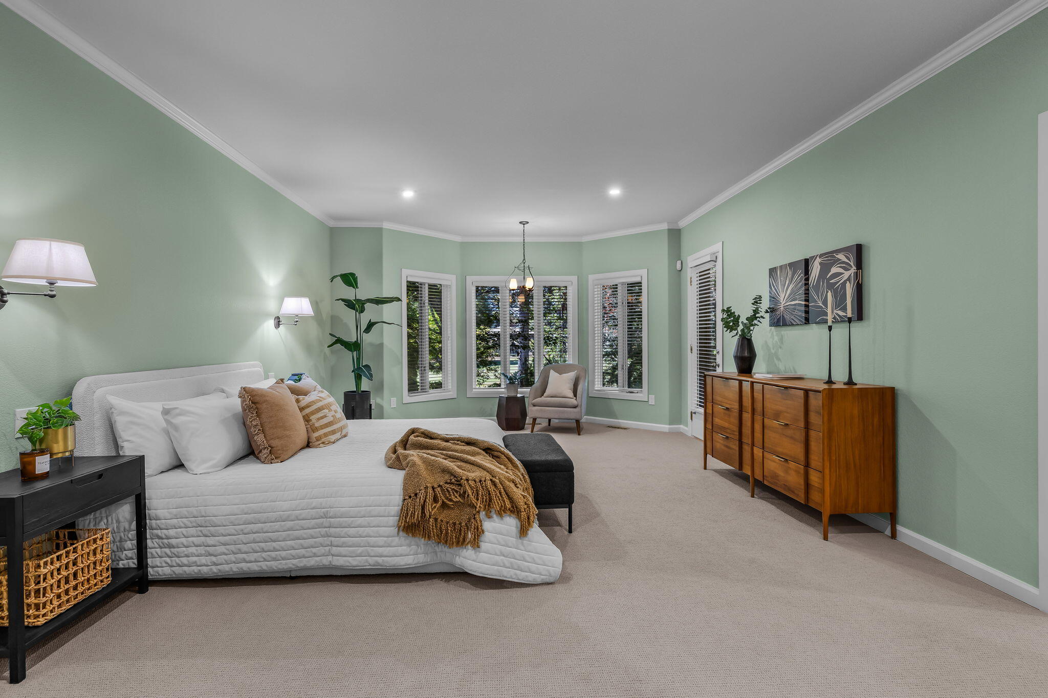 Staged bedroom with a white bed, pale green walls, shuttered windows, and a wooden dresser.