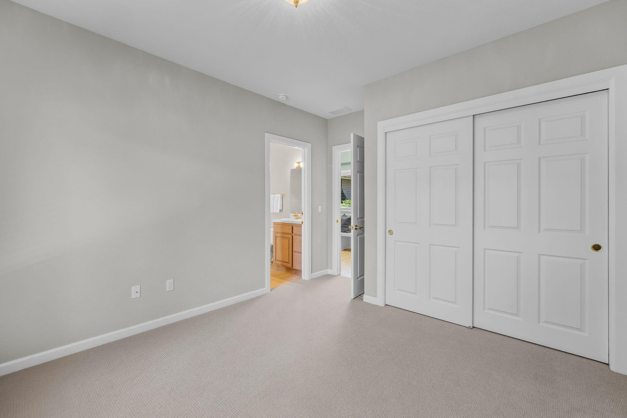 Empty carpeted bedroom with white sliding closet doors and open doorways to adjoining rooms.