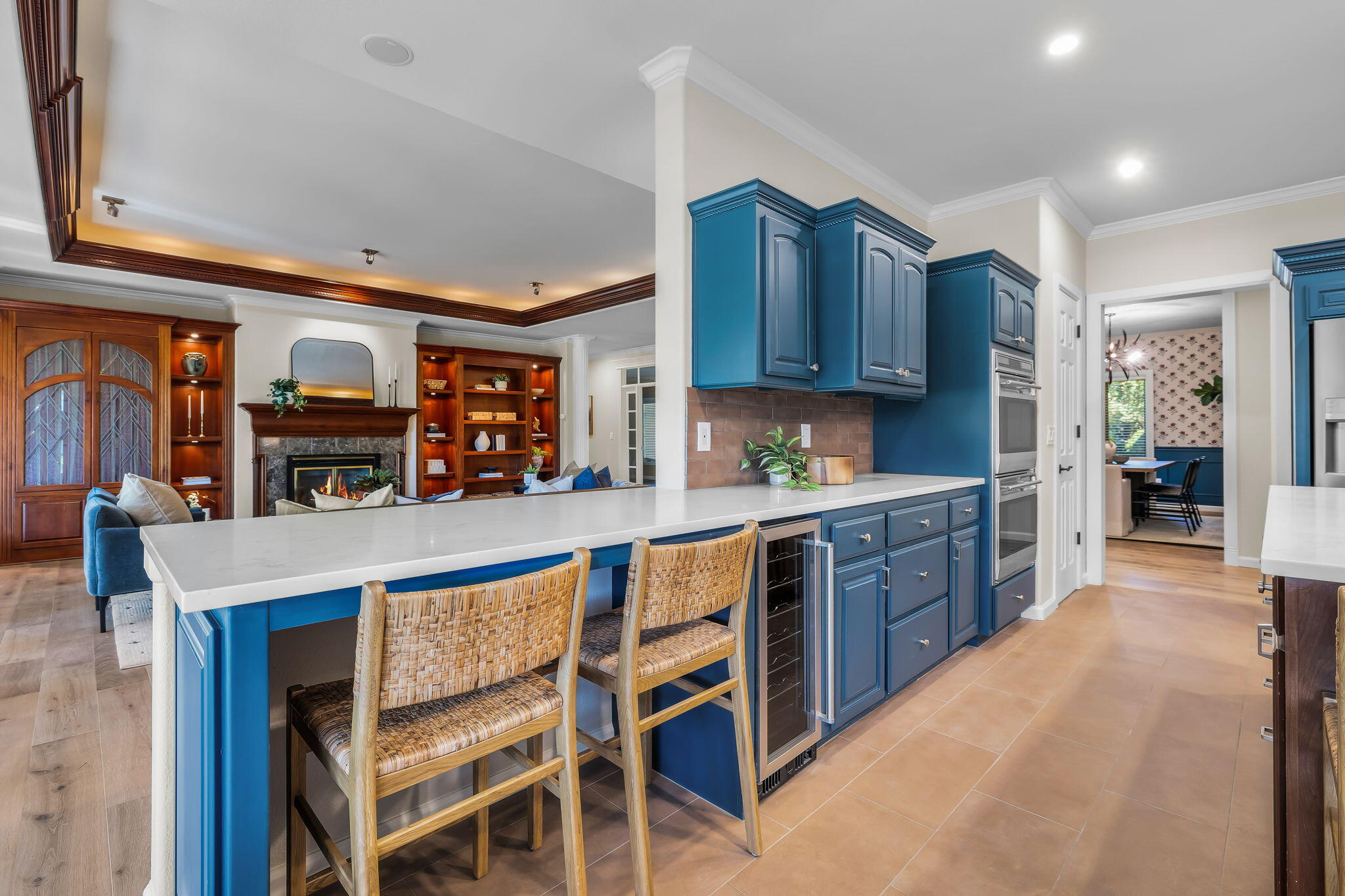 Kitchen with deep blue cabinets, a white island, woven stools and views into a living room with a fireplace.