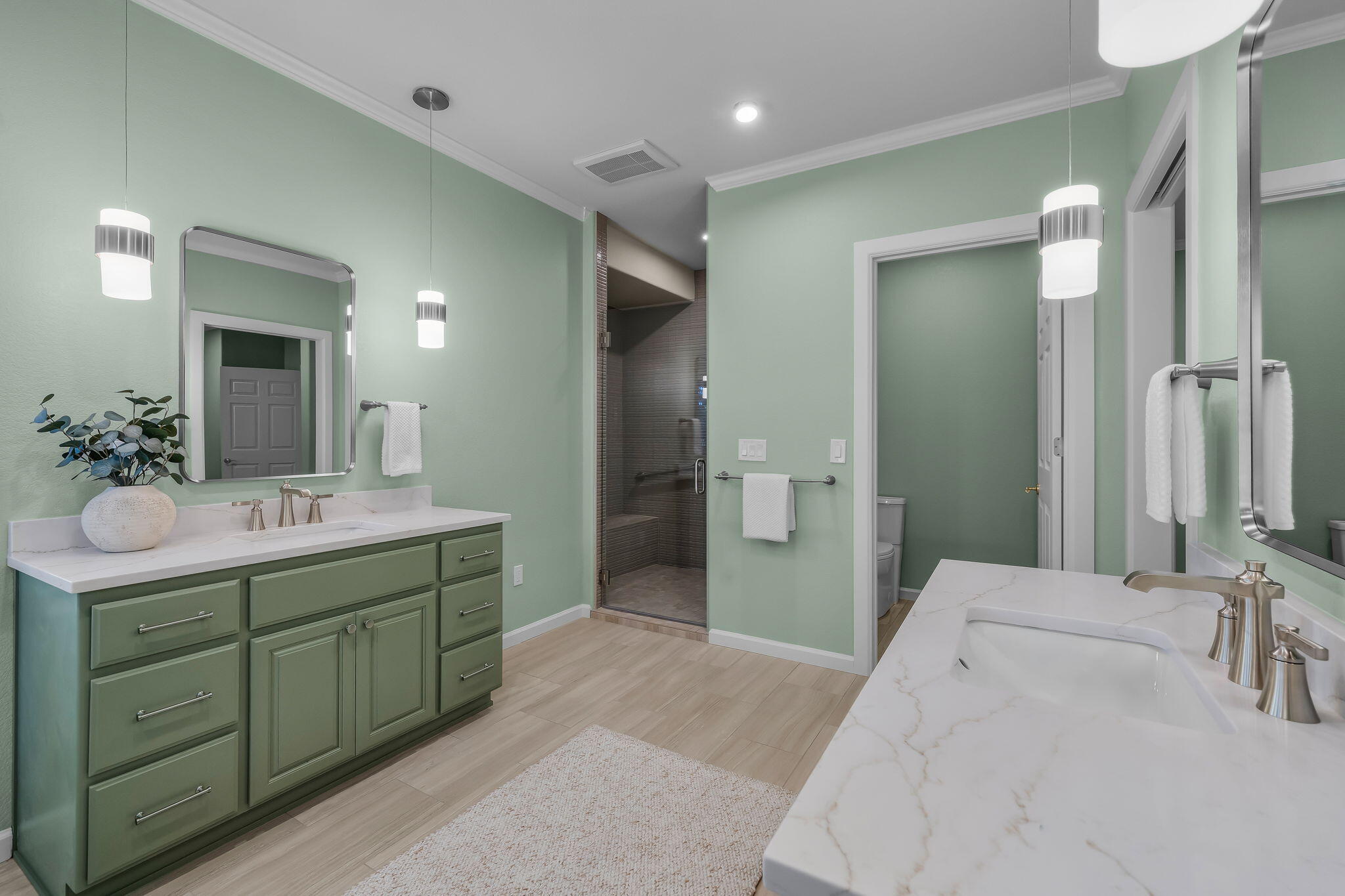 Bathroom with sage-green cabinetry, marble-look vanities, and a glass-enclosed dark-tiled shower.