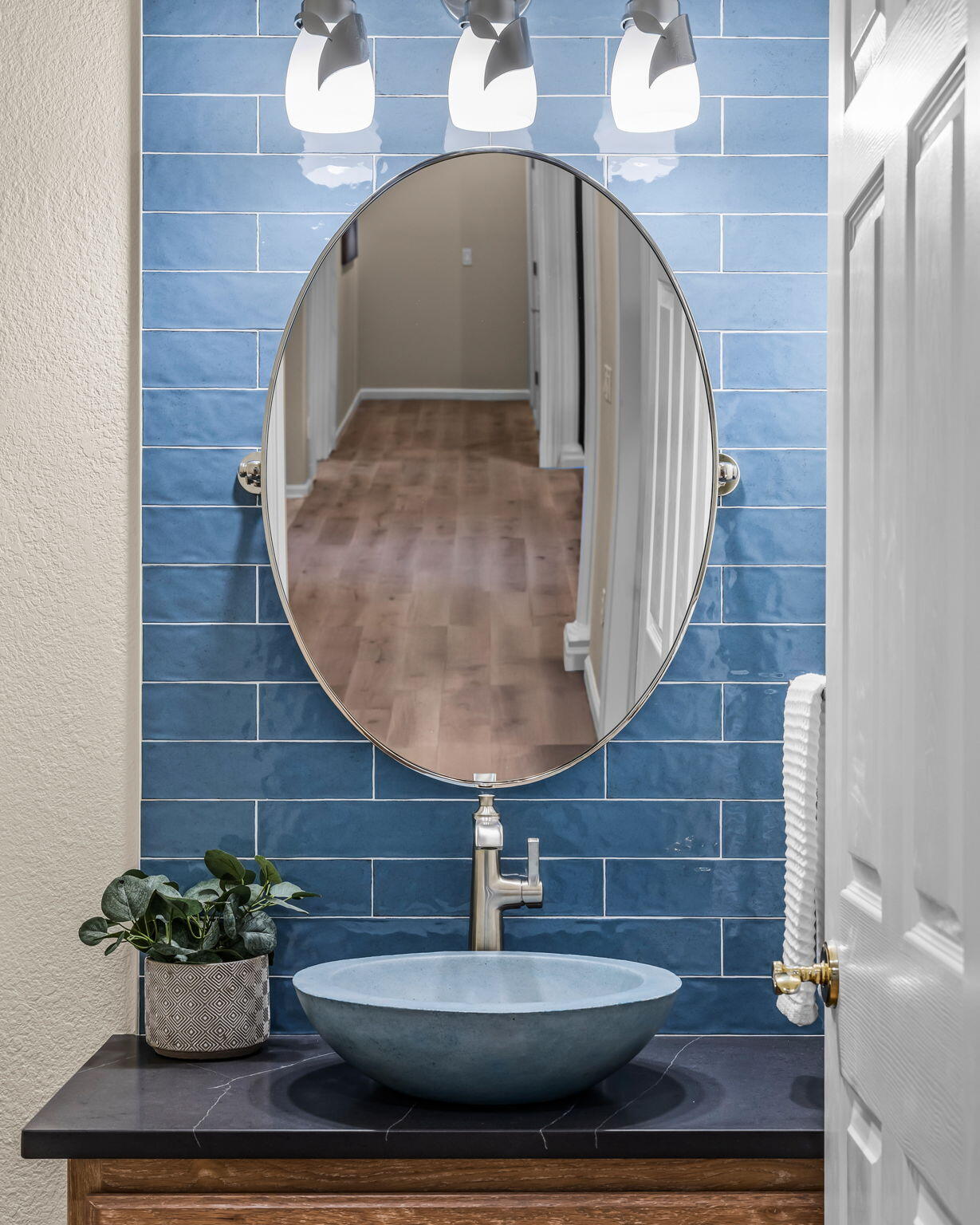 Bathroom vanity with blue tile backsplash, oval mirror, and blue vessel sink.