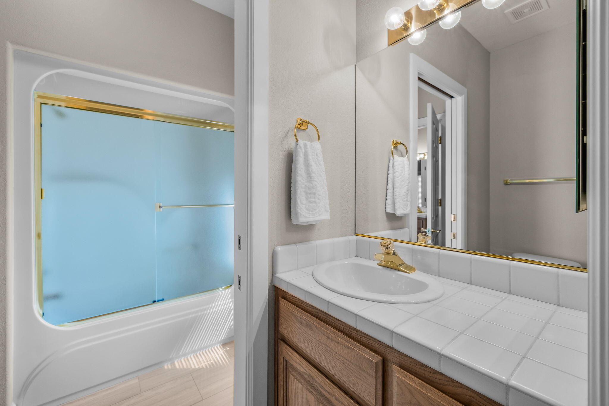 Bathroom with a blue frosted-glass tub enclosure and a tiled vanity with a gold faucet.