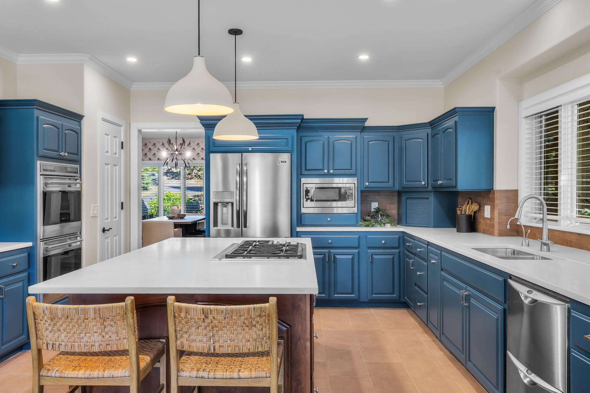 Kitchen with blue cabinets, a large cooktop island, stainless steel appliances, and woven bar chairs.