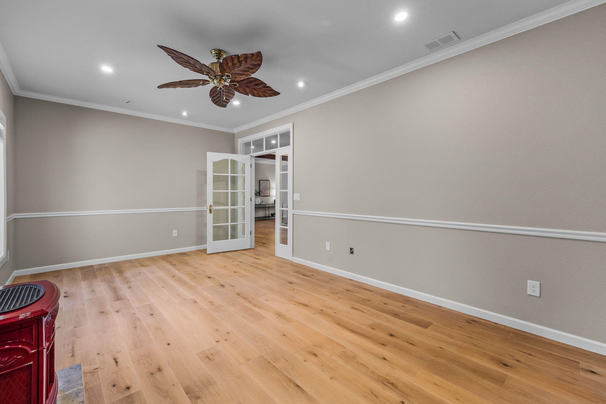 Empty room with light wood floors, French doors, and a ceiling fan with wood-patterned blades.