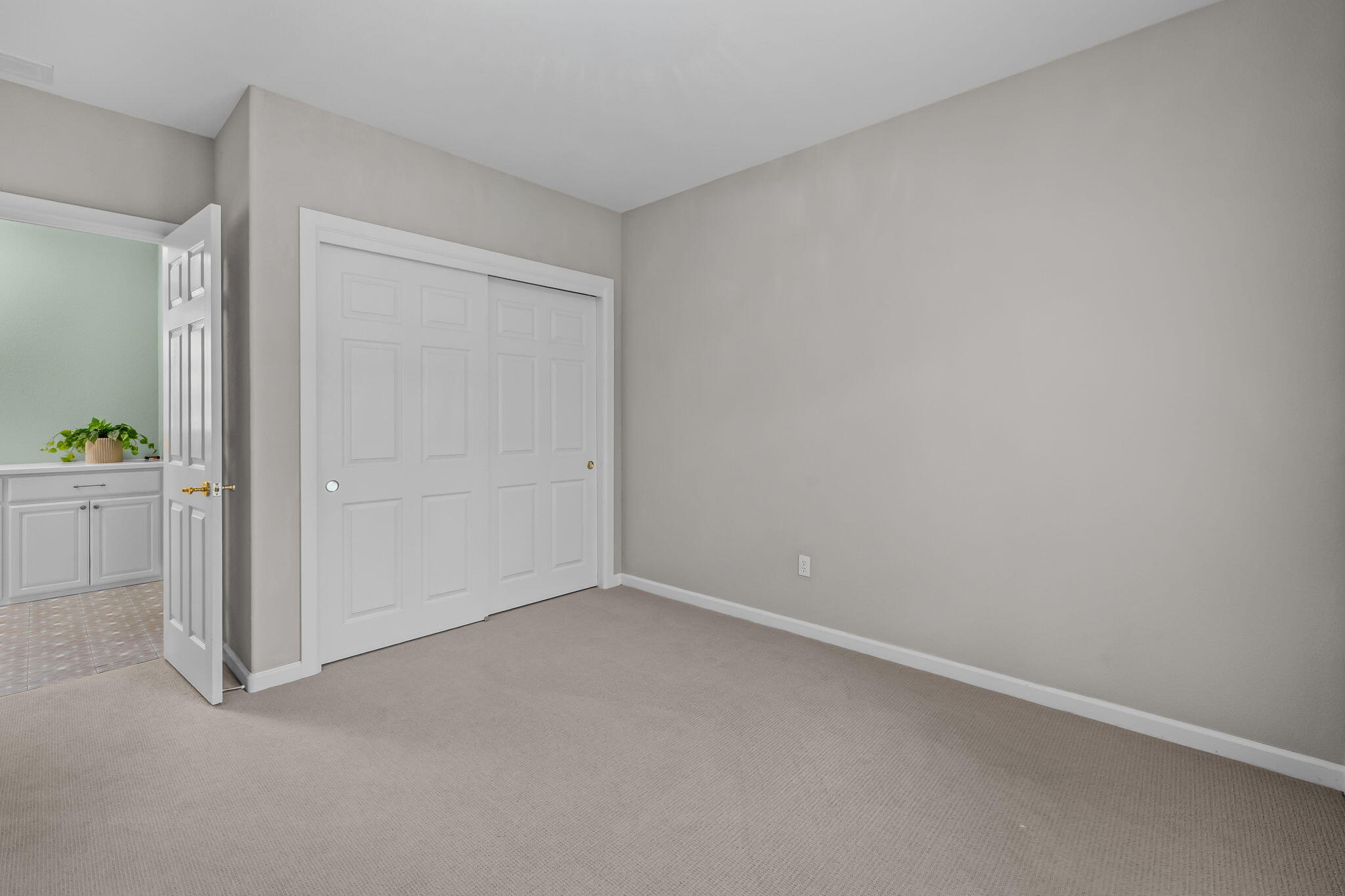 Empty bedroom with beige carpet, white closet doors, and an open doorway to a bathroom vanity.