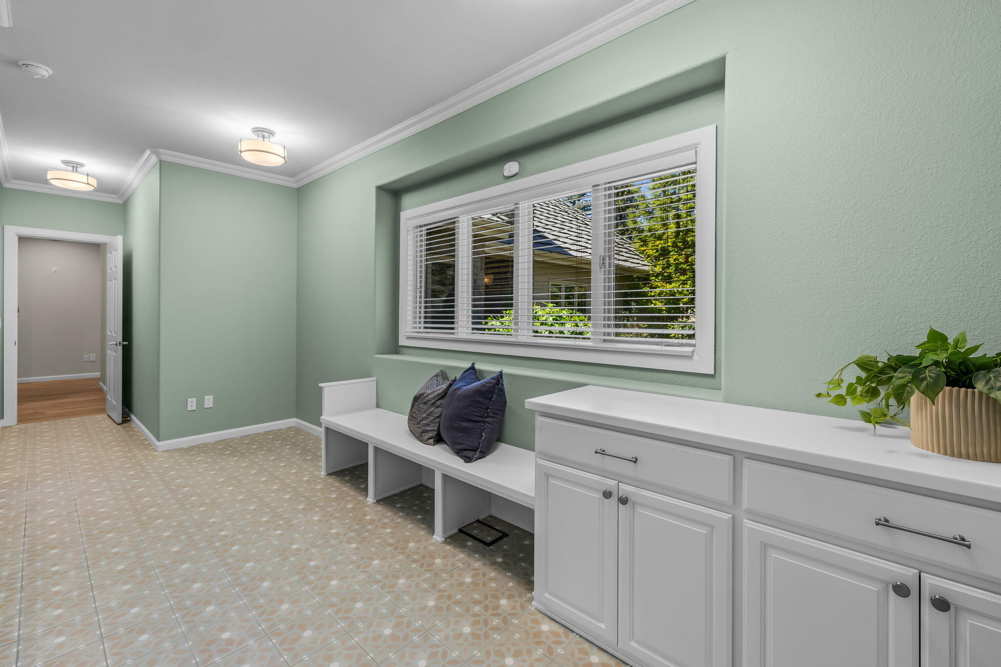 Mudroom with white built-in cabinets and bench beneath a wide window.