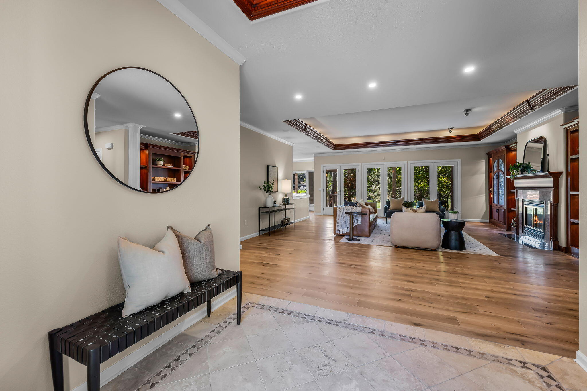 Living room with hardwood floors, a detailed tray ceiling, fireplace, and glass doors to greenery.