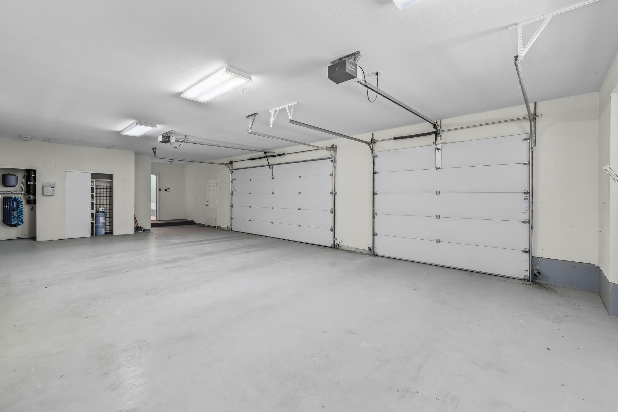 Empty three-car garage with a broad concrete floor and three white garage doors.