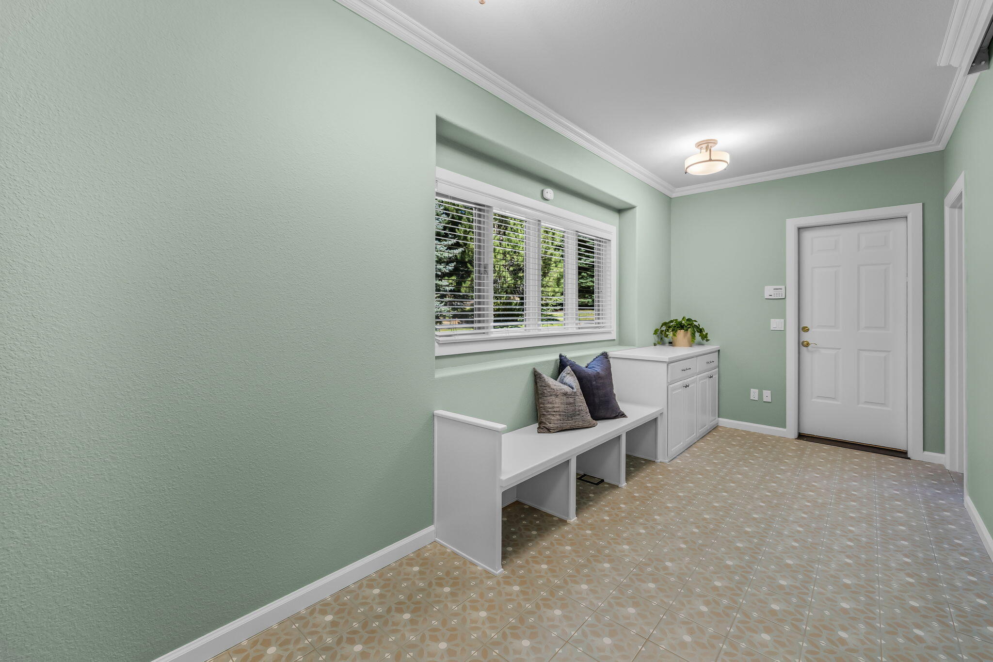 Entryway with a built-in bench, patterned tile floor, wide window, and white front door.