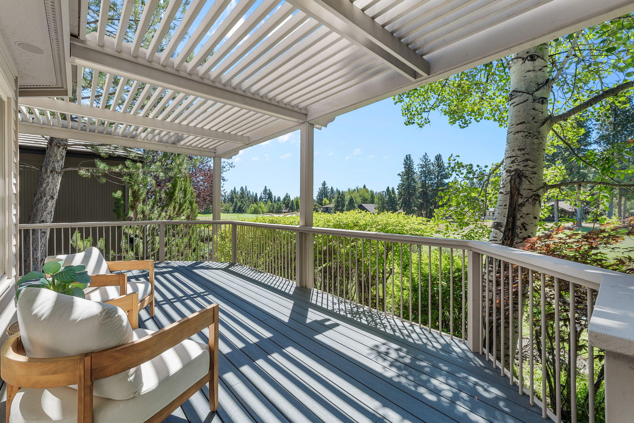 Covered deck with cushioned wooden chairs, pergola roof, and leafy views.