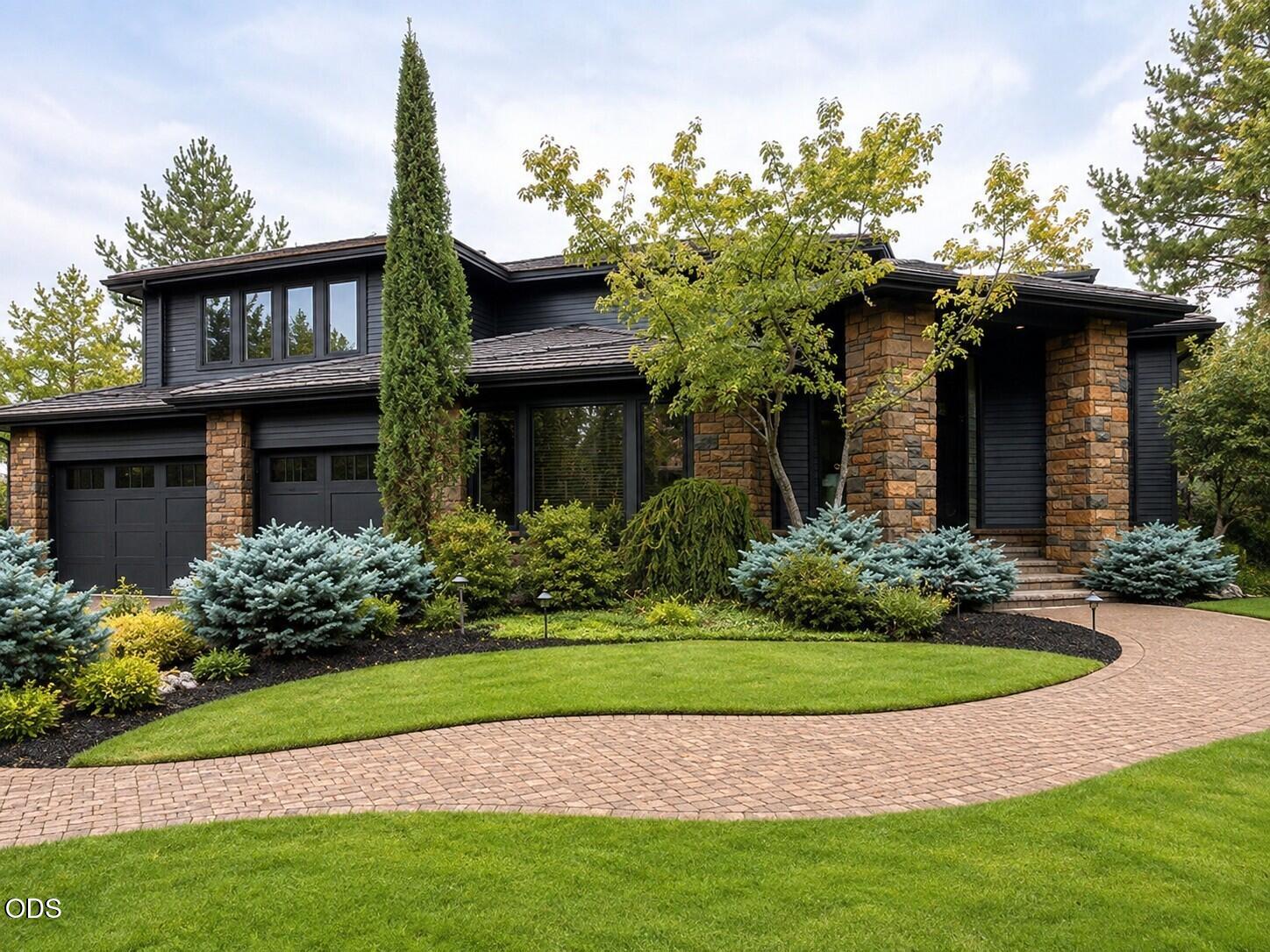 Modern dark-sided home with stone columns, two-car garage, and curved brick driveway.