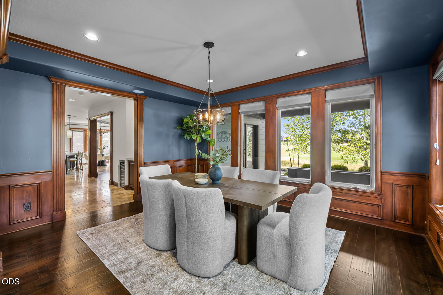 Dining room with blue walls, wood trim, a table and upholstered chairs beside large windows.