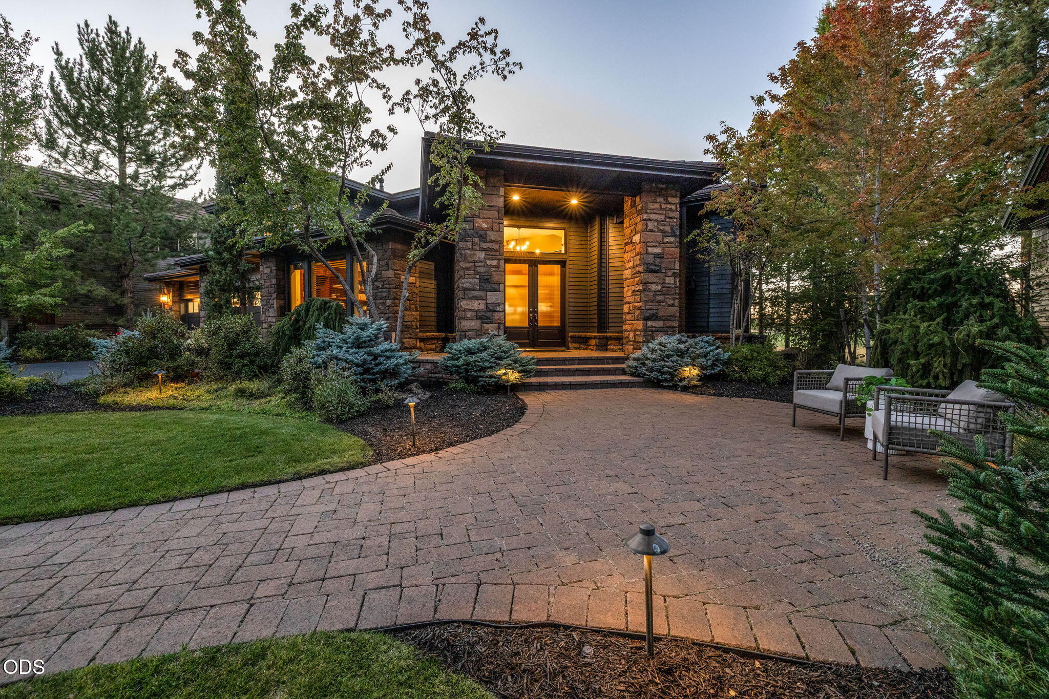 Modern stone-fronted home with a broad paver driveway and landscaped entry at dusk.