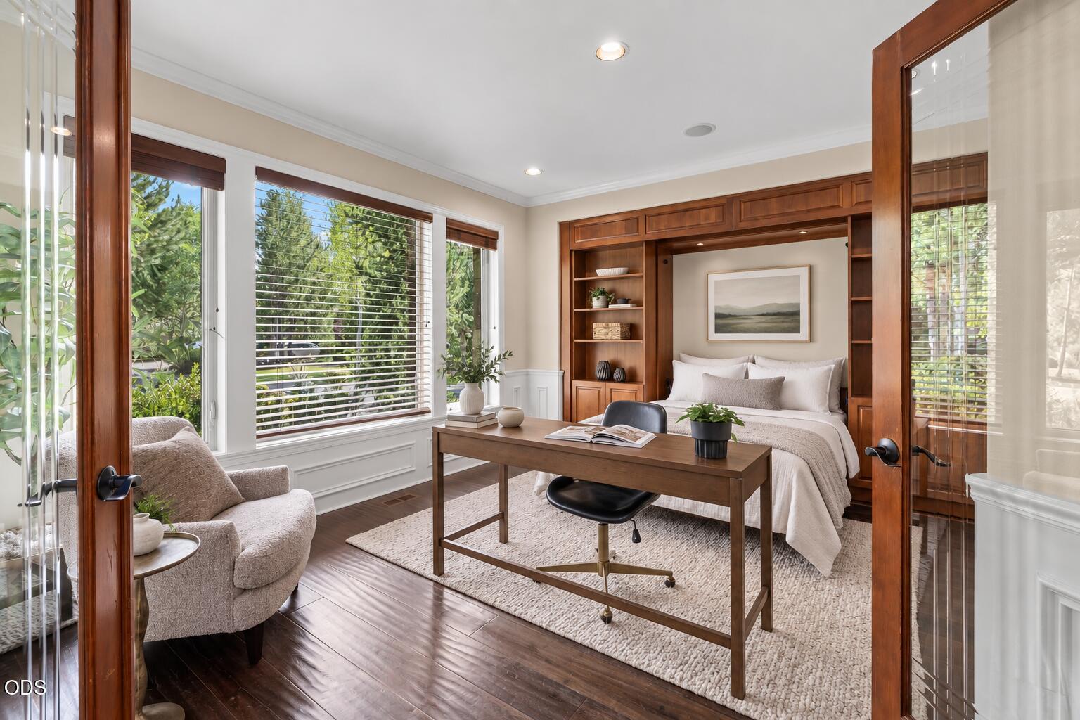 Bedroom with built-in wood shelving around the bed and a desk beside large windows.