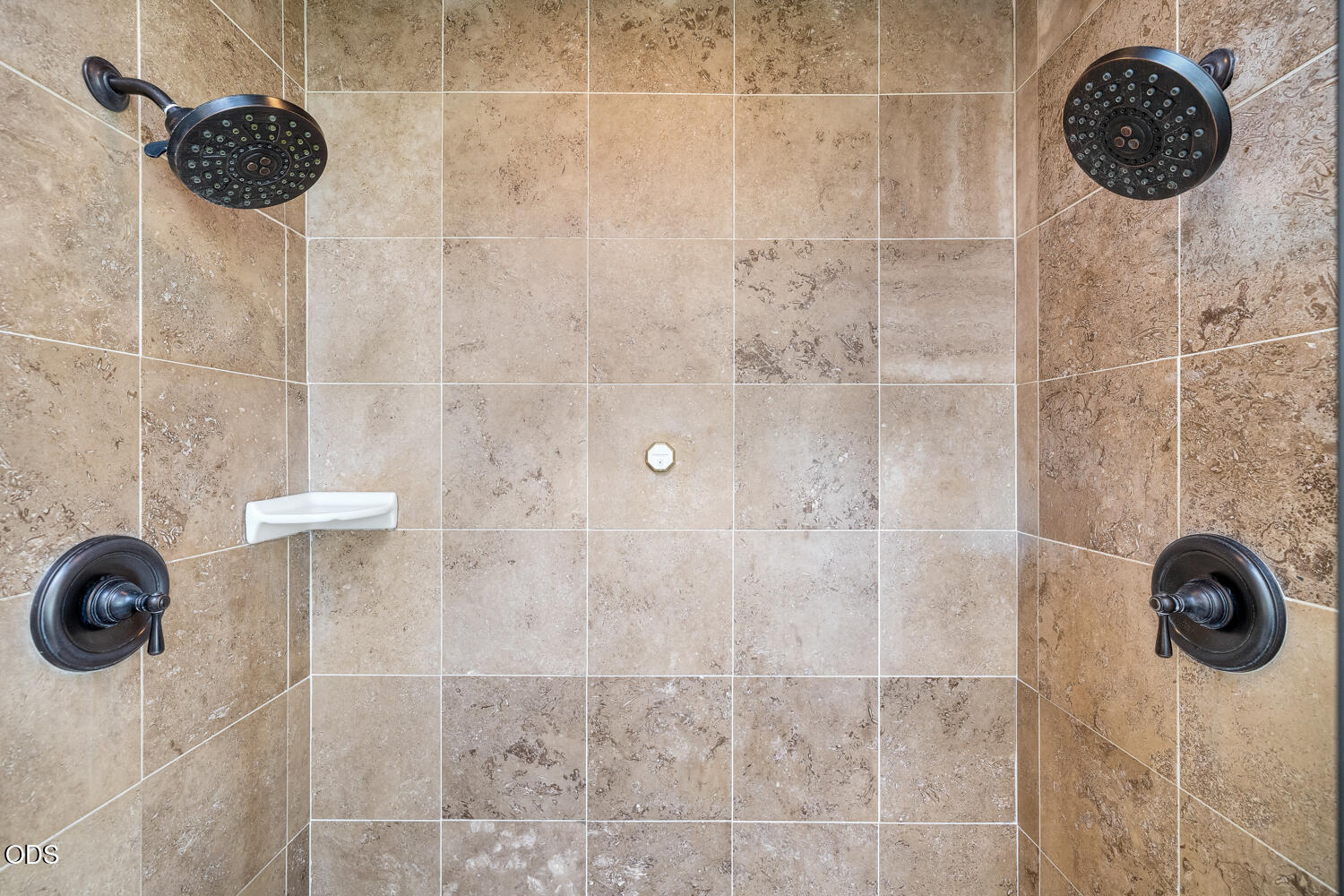 Tiled shower with two dark bronze showerheads and matching controls.