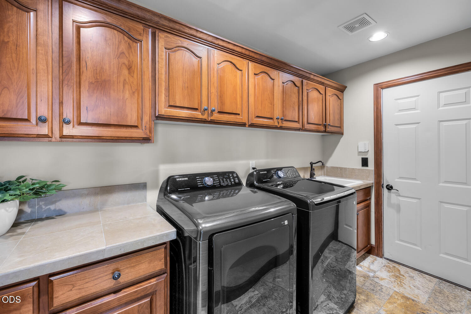 Laundry room with black washer and dryer, warm wood cabinets, and a tiled countertop.