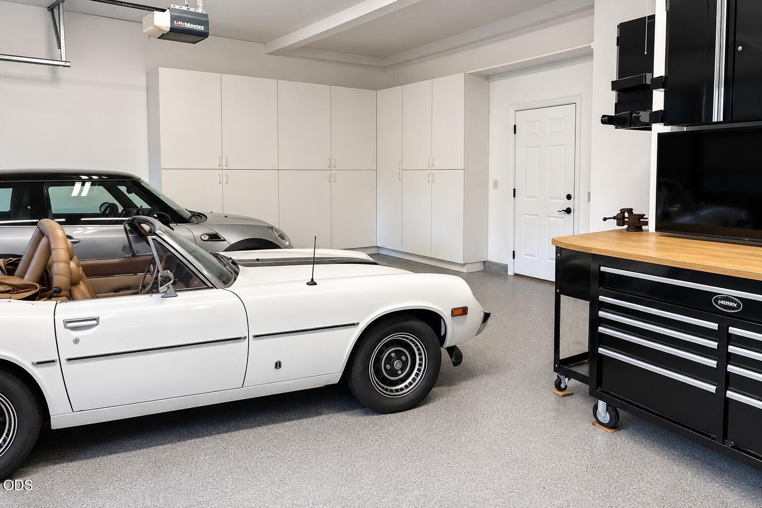 Finished garage with classic cars, extensive white storage cabinets, and a black rolling tool chest.