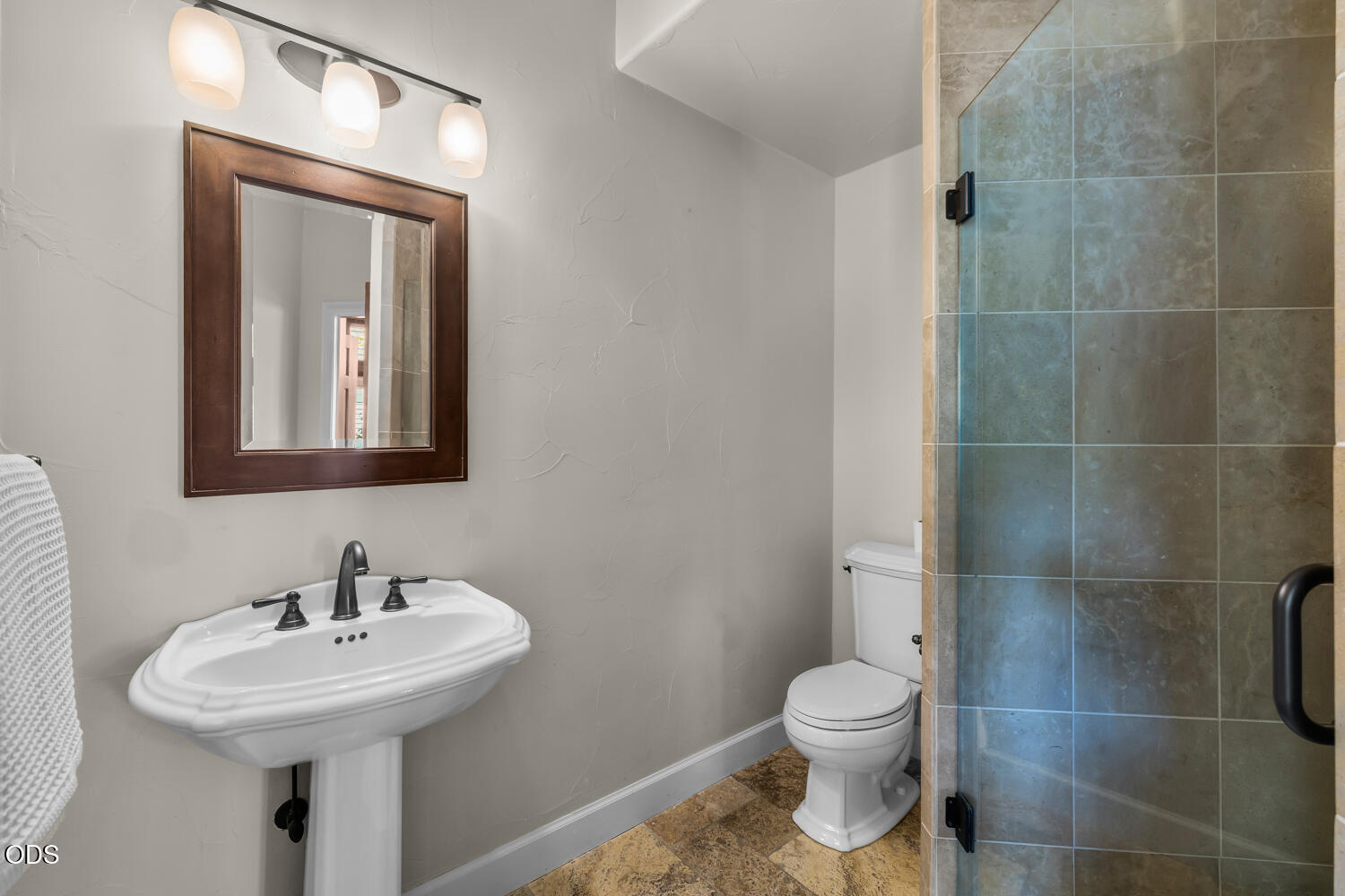 Bathroom with a pedestal sink, dark-framed mirror, toilet, and tiled glass shower.